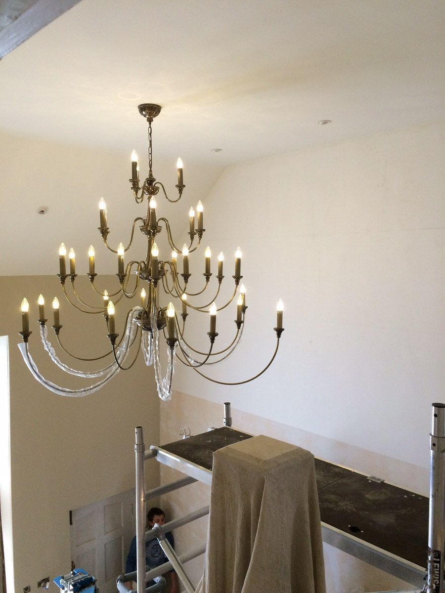 Brass candle chandelier being installed from a scaffold tower